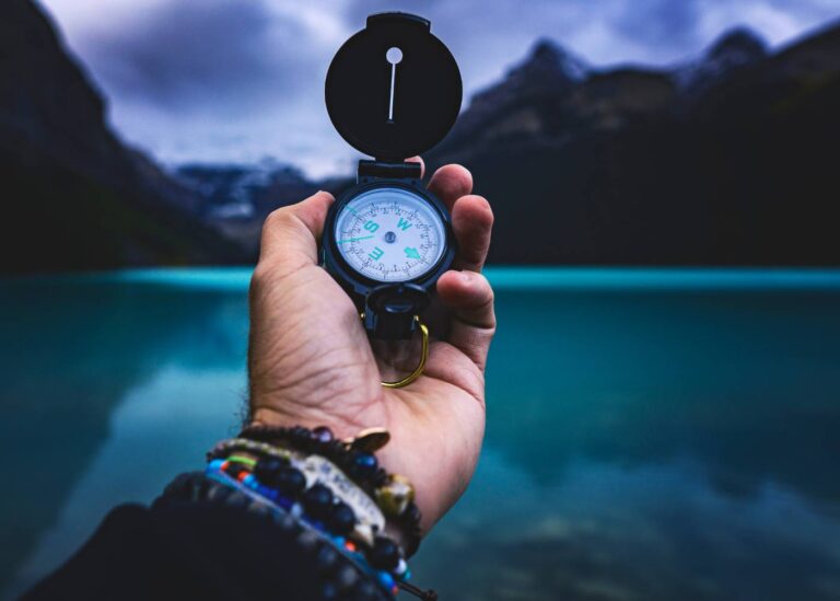 na zdjęciu kompas trzymany w dłoni w tle jezioro i las