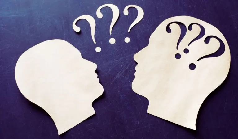 obrazek wyróżniający w artykule - dlaczego chcesz pracować w naszej firmie. Obraz przedstawia dwie stylizowane sylwetki ludzkich głów wykonane z jasnego materiału (prawdopodobnie drewna lub papieru), umieszczone na ciemnym tle. Całość kompozycji jest minimalistyczna, skupiająca się na przekazaniu idei zadawania pytań, refleksji lub poszukiwania odpowiedzi. Obraz ten może symbolizować proces myślowy, komunikację, zadawanie pytań lub refleksję, co czyni go odpowiednim do tematów związanych z nauką, edukacją, rozwojem osobistym lub zawodowym.