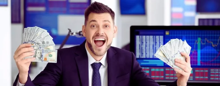 obrazek wyróżniający w artykule - ile pracodawca dostaje za pracownika z grupą inwalidzką. Na zdjęciu widać mężczyznę, który wygląda na zadowolonego i podekscytowanego. Jest ubrany w ciemny garnitur, białą koszulę i krawat. Trzyma w obu dłoniach pliki banknotów amerykańskich o nominałach 100 dolarów, pokazując je z dumą w stronę aparatu. Ma szeroko otwarte usta, jakby wyrażał radość lub zaskoczenie, co może sugerować, że jest podekscytowany z powodu zarobionych pieniędzy. W tle widać ekrany komputerowe, na których wyświetlane są wykresy i dane, co może sugerować, że mężczyzna jest w środowisku związanym z finansami, inwestycjami lub giełdą. Kolory na ekranach to głównie niebieskie i czerwone, charakterystyczne dla wykresów finansowych.